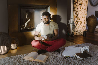 Young man listening to music while reading book at home