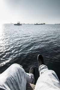 Low section of men sitting by sea against sky