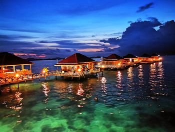 Illuminated buildings by sea against sky at night