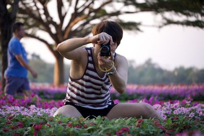 Rear view of man on purple flowering plants on field holding camera