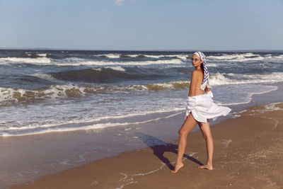 Woman in a white bathing suit and hat sunglasses on an empty sandy beach