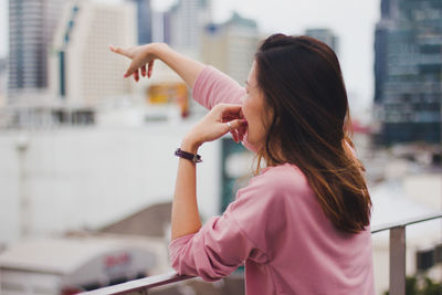 Woman standing against railing pointing at city