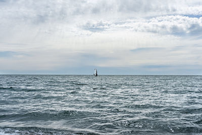 Athlete riding windsurf in the distance on blue sea against cloudy sky in summer, water sports
