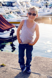 Fashionable boy wearing sunglasses and a hairstyle at the pier with yachts at sunset