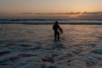 Rear view of man walking into the water with surfboard