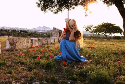 Full length of woman with poppy sitting on field