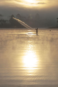 Silhouette man standing in sea against sky during sunset