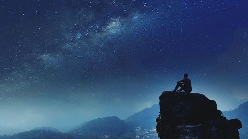 Low angle view of man sitting on cliff against star field