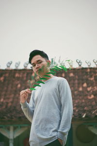 Portrait of young man holding camera against clear sky