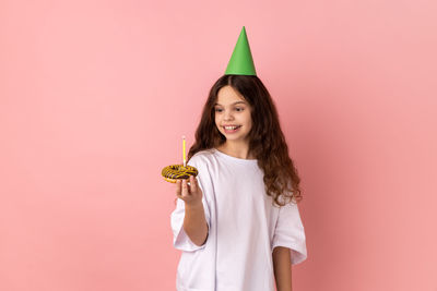 Portrait of young woman with arms raised against pink background