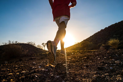 Low section of man standing on land against sky during sunset