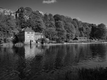 Reflection of building and trees by lake against sky