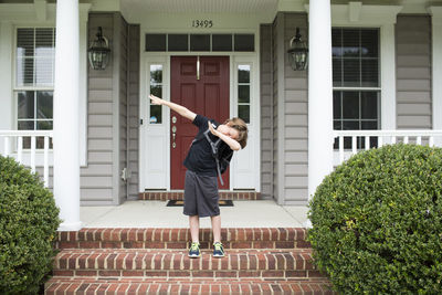 Tween boy dabs on front porch of his house, standing on brick steps