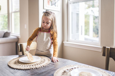 Little girl in apron flipping pancake at breakfast table