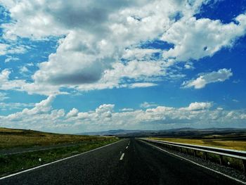 Road passing through field against cloudy sky