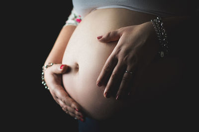 Midsection of woman touching hair over black background