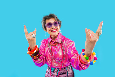 Portrait of smiling woman with arms raised standing against blue background