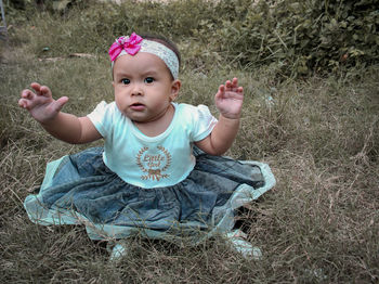 Portrait of cute baby girl sitting on land