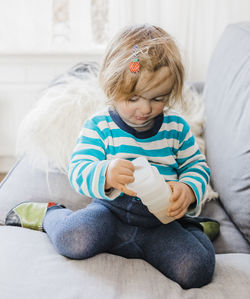 Full length of cute girl with container kneeling on sofa at home