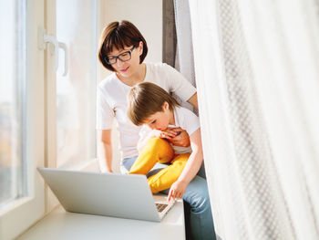 Mother and son looking at laptop by window