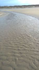 Surface level of wet sand on beach against sky