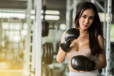 Portrait of confident young woman with boxing gloves standing in gym