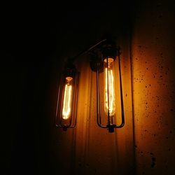 Close-up of illuminated light bulb hanging against black background