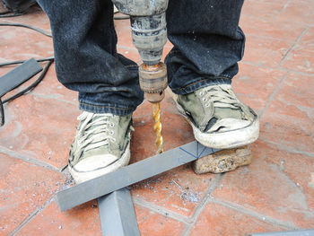 Low section of worker drilling metal on walkway 