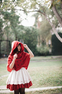 Woman in little red riding hood costume standing by plants