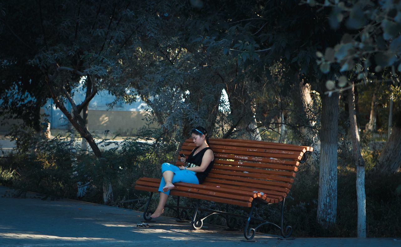 tree, full length, lifestyles, leisure activity, sitting, relaxation, bench, casual clothing, rear view, childhood, person, park - man made space, day, side view, outdoors, tree trunk, elementary age