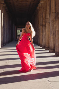 Full length of young woman in pink evening gown walking at colonnade