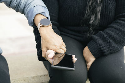 Two spanish-latin women with smartphones and smartwatches, selective focus on the clipped hands.