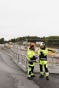 Male engineers in reflecting clothing talking at building site