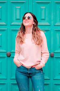 Young woman wearing sunglasses while standing against turquoise door