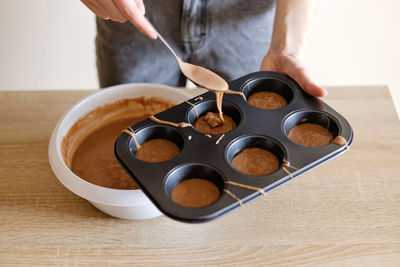 Young woman pours chocolate dough into cupcake molds