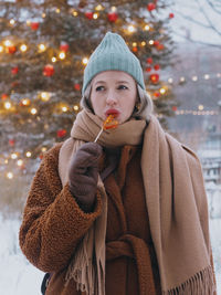 Young stylish woman eating rooster shaped lollipop on a christmas market.