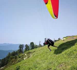 Side view of men paragliding against sky