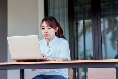 Young woman using phone while sitting on table