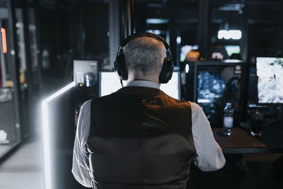 Rear view of elderly man playing video game on computer at gaming lounge