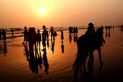 Silhouette people on beach against sky during sunset