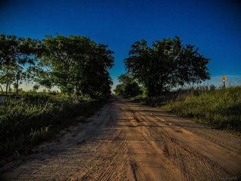 Dirt road passing through landscape against clear blue sky