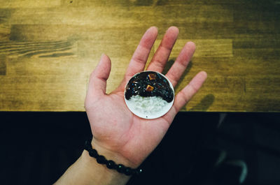 Cropped hand of man holding small plate with rice and curry over wooden table