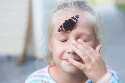 A beautiful black butterfly with orange spots, sits on a forehead of a caucasian girl of 7-8 years