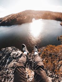 Low section of man sitting on cliff against lake