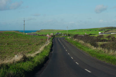 Empty road amidst field against sky