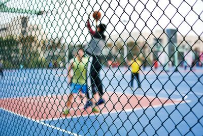 Men seen through chainlink fence against sky