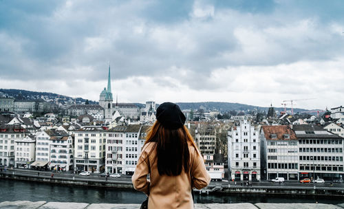 Rear view of woman looking at cityscape against cloudy sky