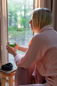 A woman drinks herbal tea in the living room and looks out the window.