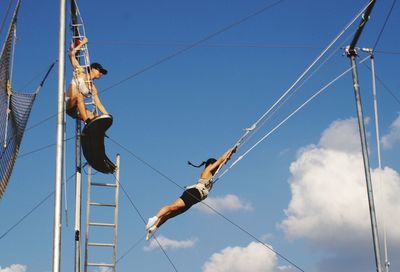 Low angle view of man hanging on rope against sky