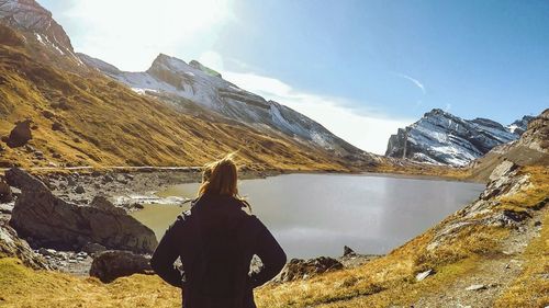 Rear view of woman standing by lake against mountains